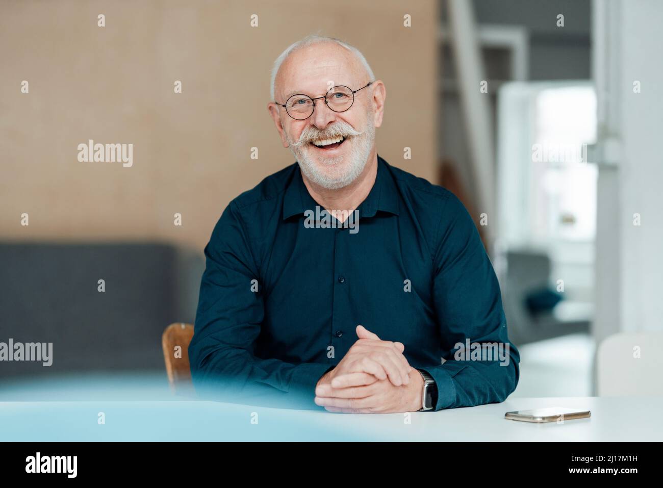 Fröhlicher Geschäftsmann, der mit den Händen am Tisch im Büro sitzt Stockfoto