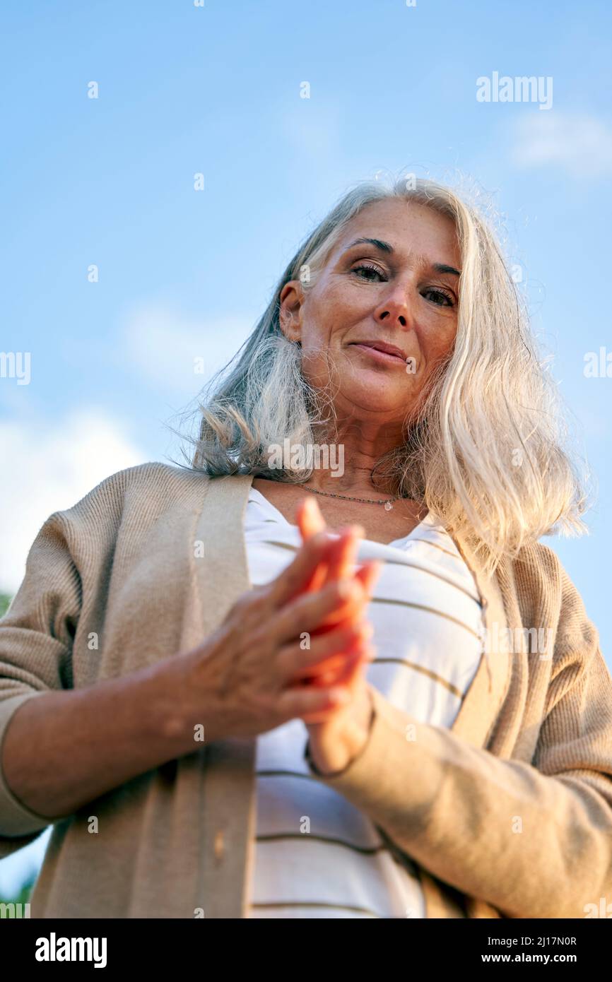 Lächelnde Frau, die mit zusammengekrallten Händen steht Stockfoto