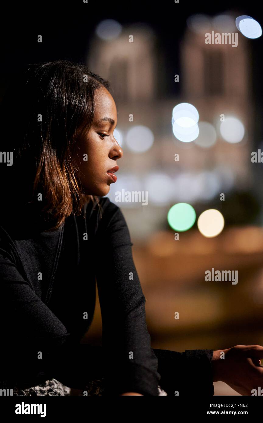 Junge Frau in schwarzem Kleid sitzt auf dem Fußweg in der Nacht Stockfoto