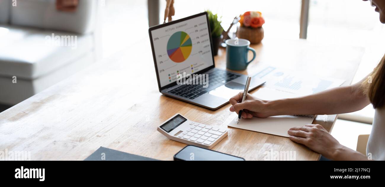 Nahaufnahme von weiblichen Händen mit Laptop-Computer und Stift, die Notizen machen, während sie mit Kalkül zu Hause rechnen Stockfoto