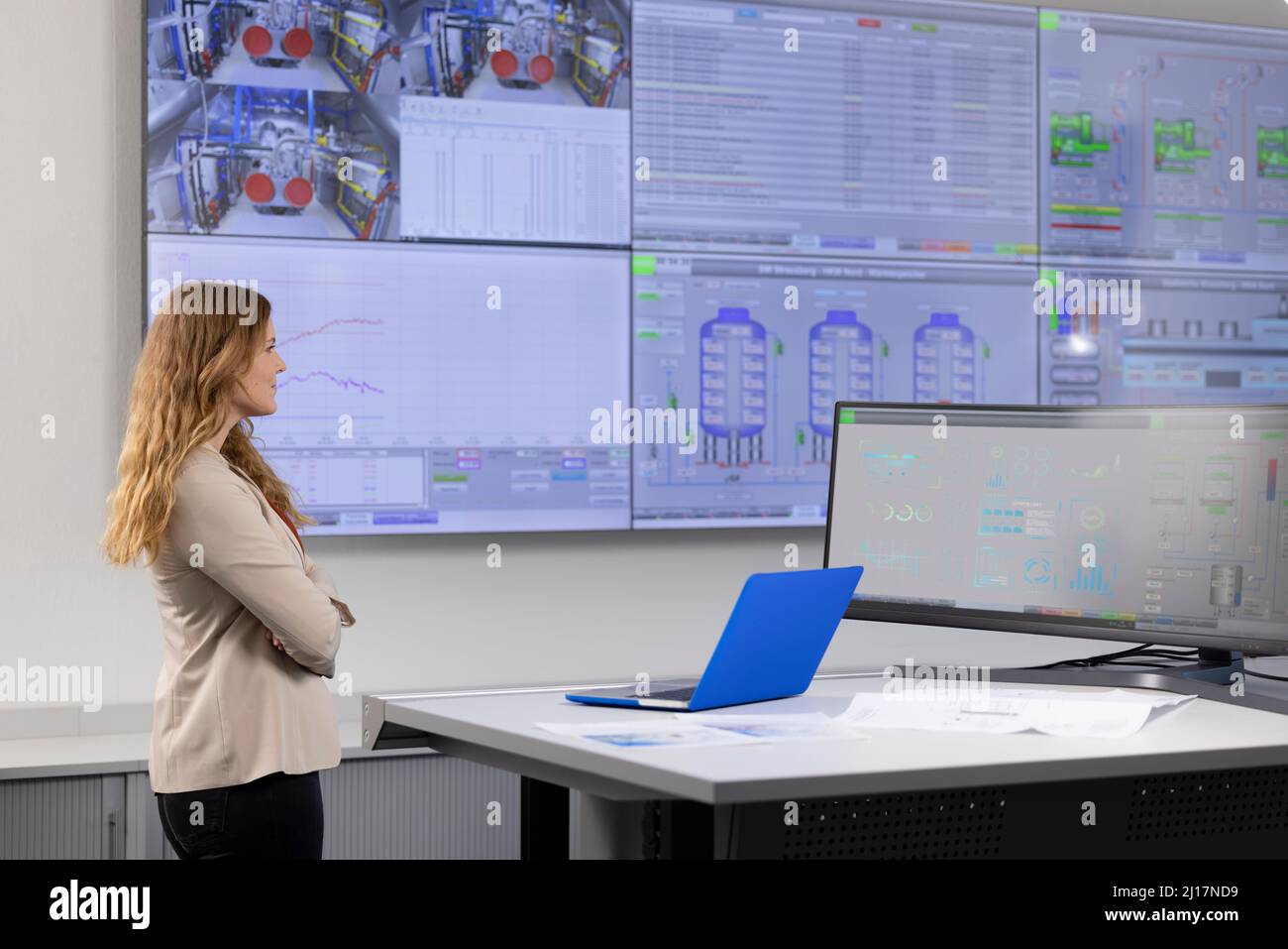 Geschäftsfrau mit gekreuzten Armen und Blick auf den Computerbildschirm im Kontrollraum Stockfoto