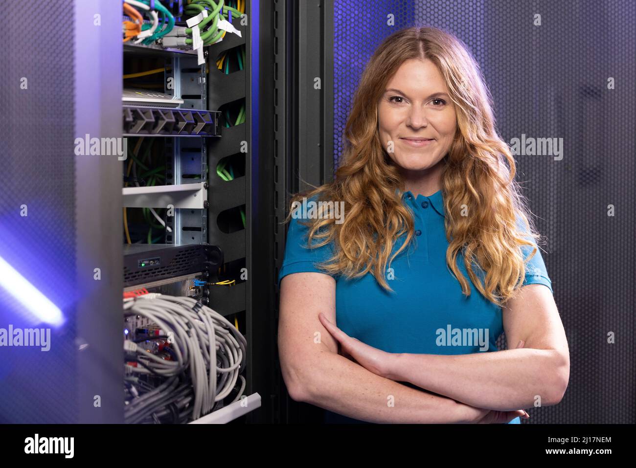 Glücklicher Techniker, der mit gekreuzten Armen im Serverraum steht Stockfoto