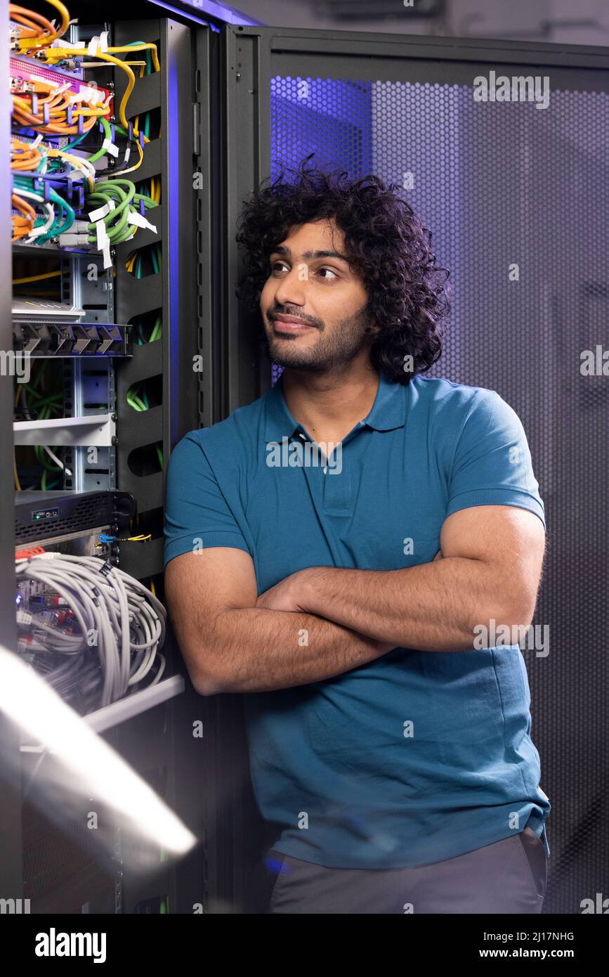 Lächelnder IT-Techniker, der mit gekreuzten Armen im Serverraum in der Industrie steht Stockfoto