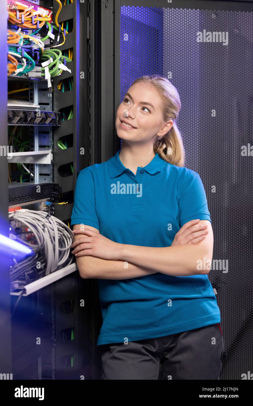 Lächelnder Techniker, der mit gekreuzten Armen im Serverraum bei der Industrie steht Stockfoto