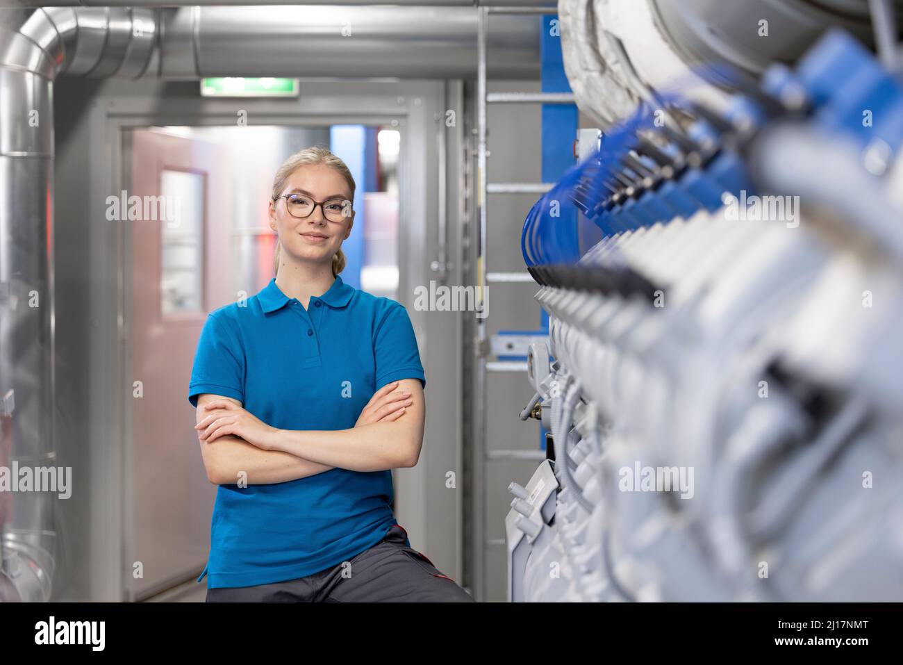 Glücklicher Techniker, der mit gekreuzten Armen im Werk steht Stockfoto
