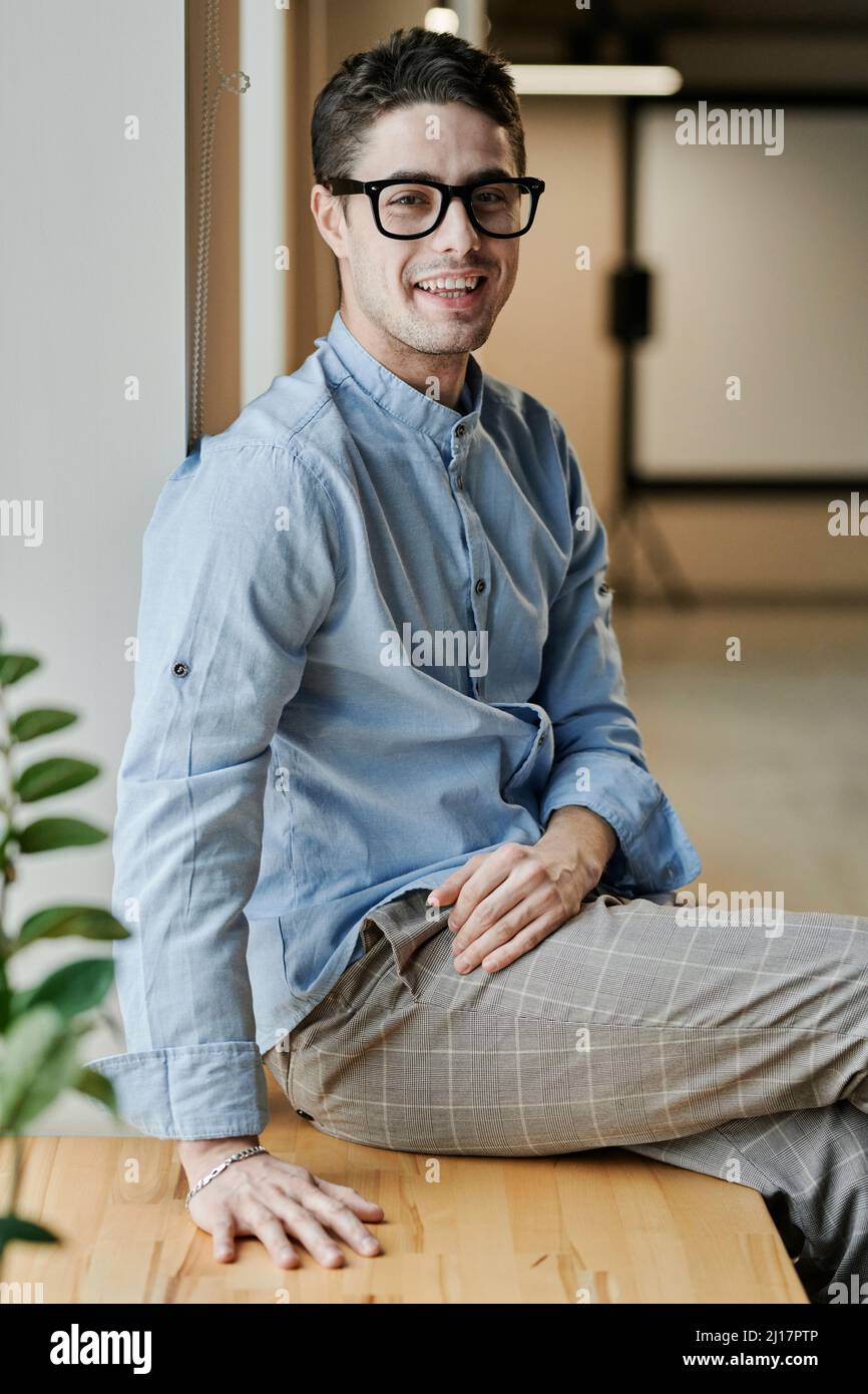 Fröhlicher Geschäftsmann, der im Büro auf dem Tisch sitzt Stockfoto