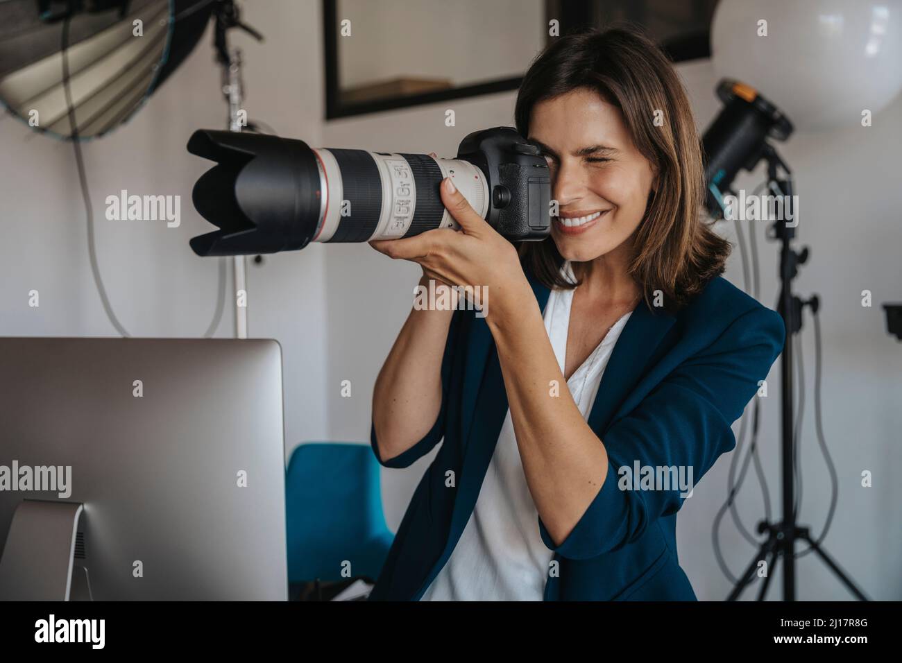 Lächelnder Fotograf, der im Studio durch die Digitalkamera fotografiert Stockfoto