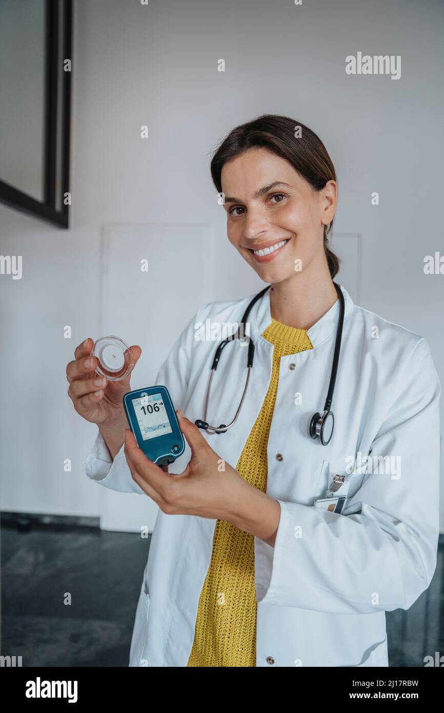 Lächelnder Arzt, der das Blutzuckermessgerät in der Klinik hält Stockfoto