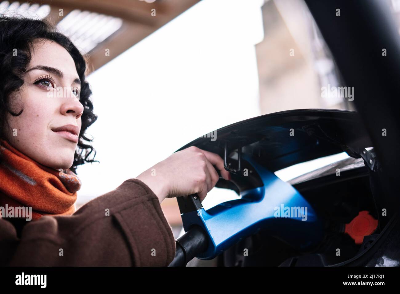 Junge Frau mit Ladegerät für Elektroautos an der Ladestation Stockfoto