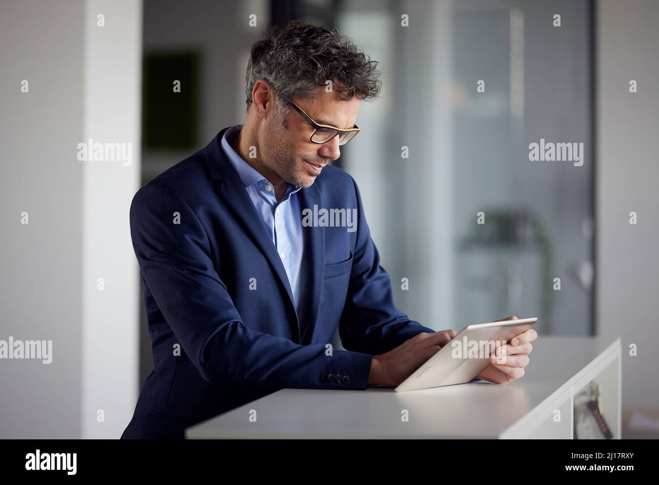 Geschäftsmann mit Brille und Tablet-PC, der im Büro am Schreibtisch steht Stockfoto