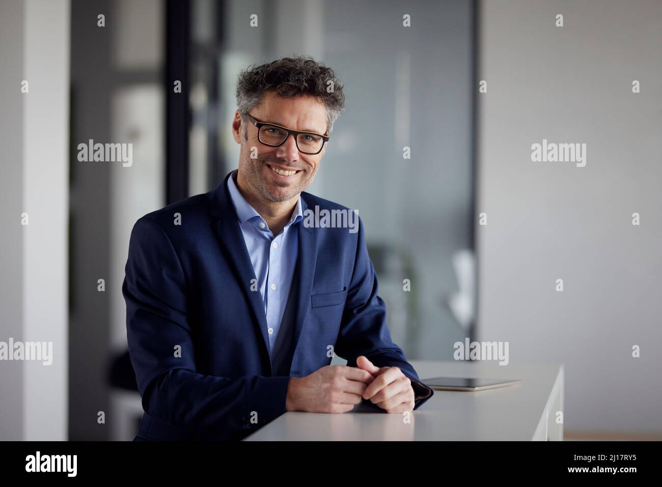 Ein glücklicher Geschäftsmann, der eine Brille trägt und am Schreibtisch im Büro steht Stockfoto