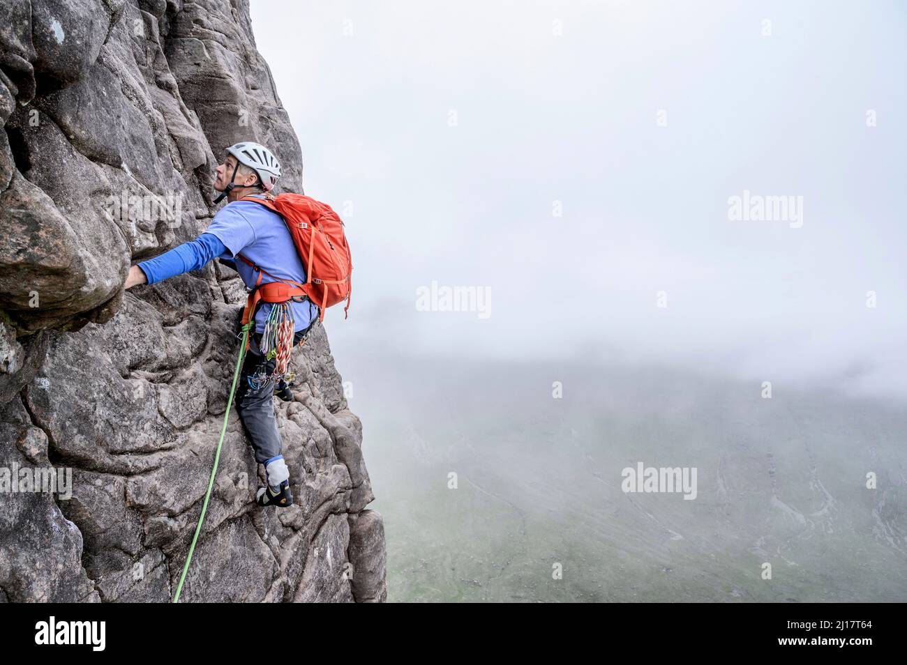 Mann mit Helm klettert auf felsigen Berg Stockfoto