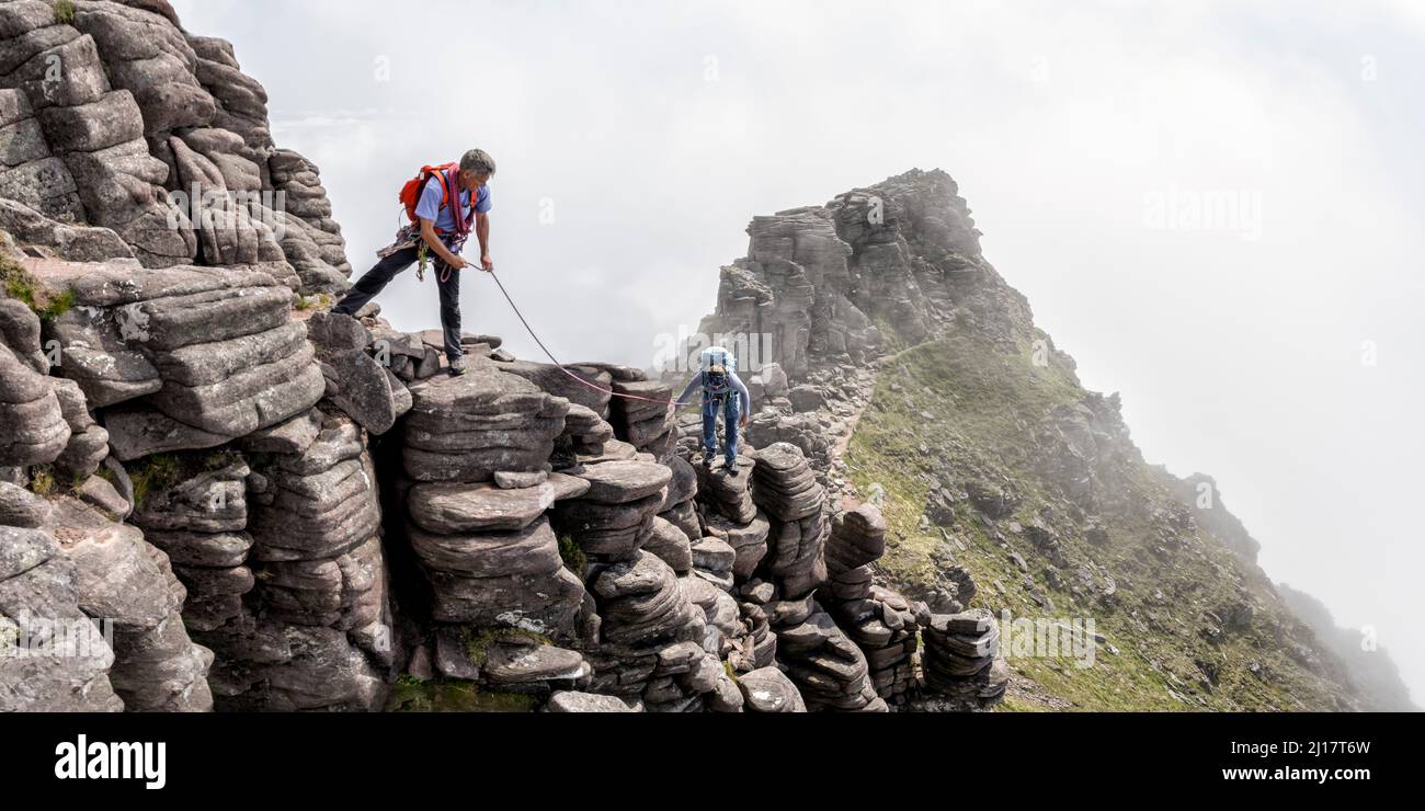 Mann, der der Frau mit einem Seil beim Aufstieg auf den felsigen Berg half Stockfoto