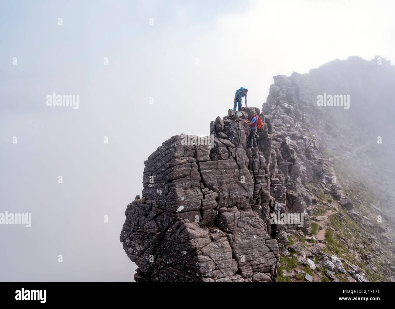 Mann, der der Frau hilft, den felsigen Berg zu erklimmen Stockfoto