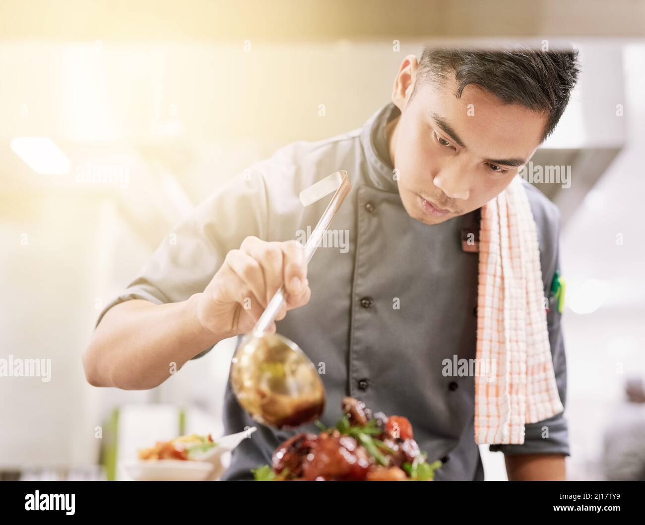 Der letzte Schliff. Eine kleine Aufnahme eines jungen Küchenchefs, der in seiner Küche kocht. Stockfoto