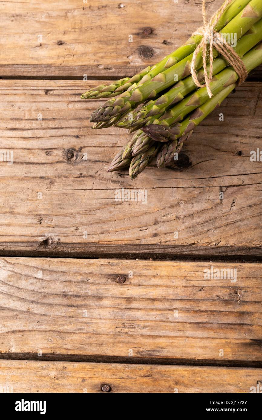 Ansicht von oben auf einem braunen Holztisch mit Schnur gebundenen rohen grünen Spargelbüschen Stockfoto