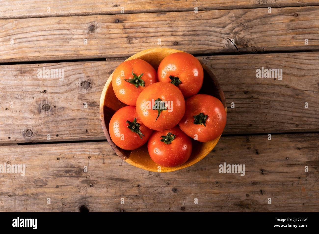 Blick von oben auf Wassertropfen auf frischen roten Tomaten auf dem Teller über dem Holztisch Stockfoto