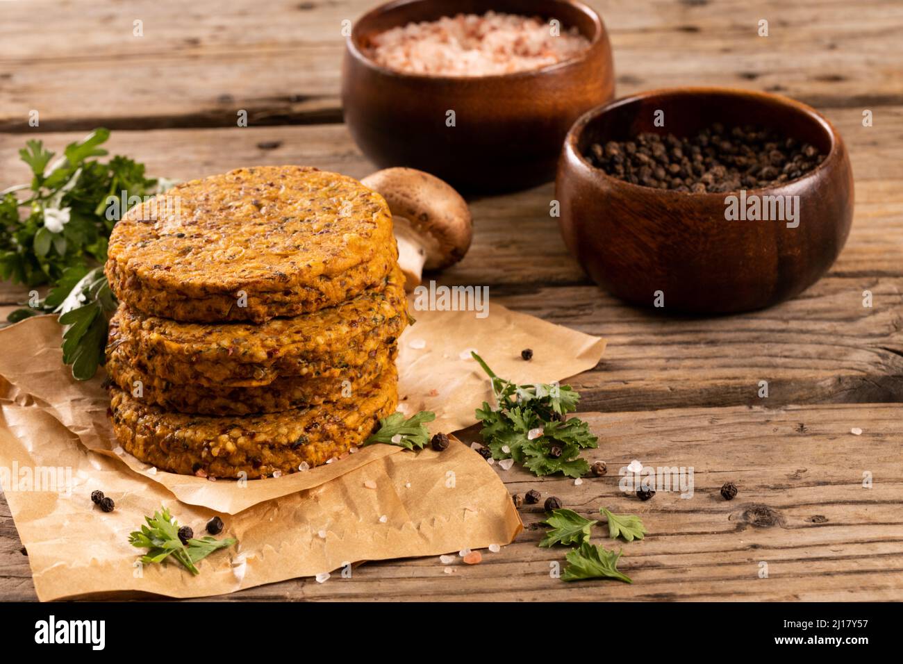 Gestapelte frische Hacksteaks auf Wachspapier mit Gewürzschüsseln auf Holztisch Stockfoto