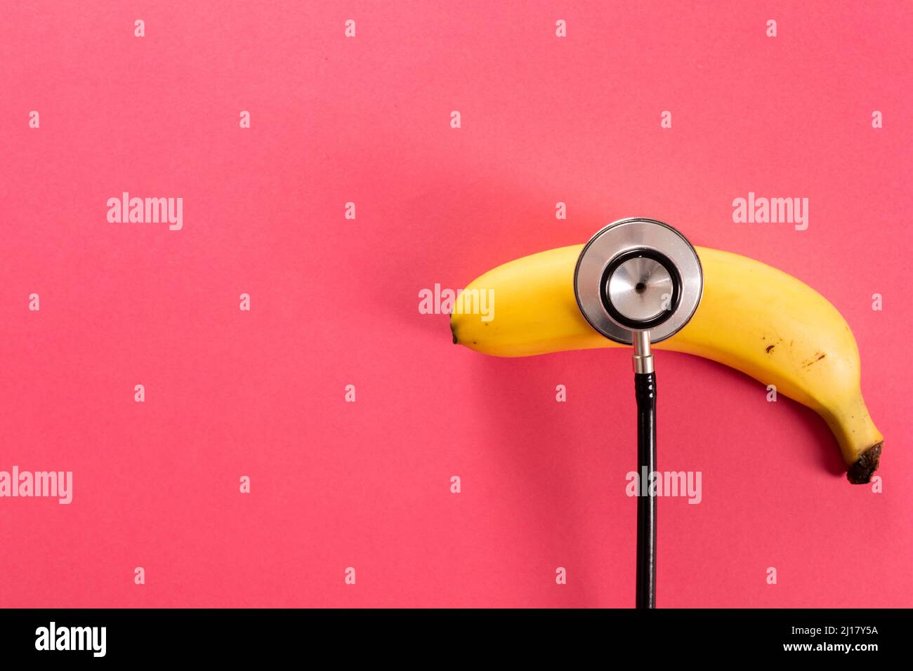 Overhead-Ansicht der frischen Banane mit Stethoskop durch Kopierraum auf rosa Hintergrund Stockfoto