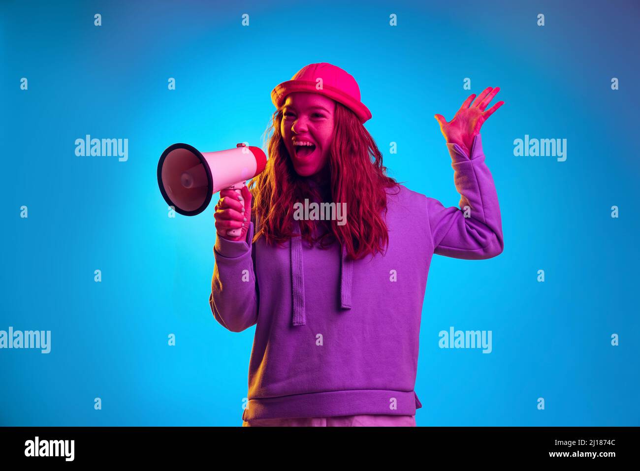 Porträt eines jungen gefühlvollen Mädchens, das auf einem Megaphon spricht, das auf blauem Studiohintergrund in pinkem Neonlicht isoliert ist Stockfoto