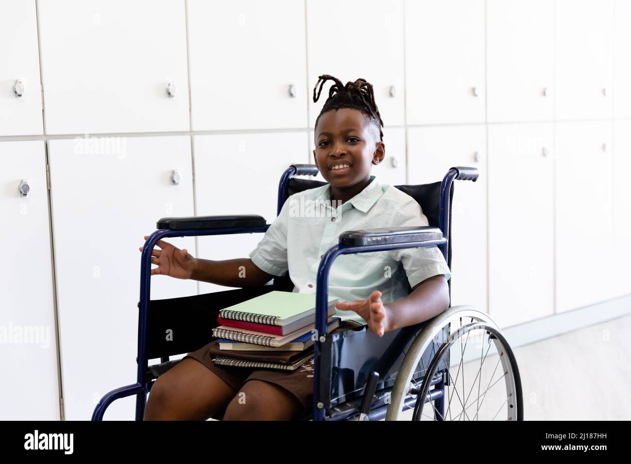 Porträt eines lächelnden afroamerikanischen Grundschuljungen mit Büchern, die auf einem Rollstuhl sitzen Stockfoto