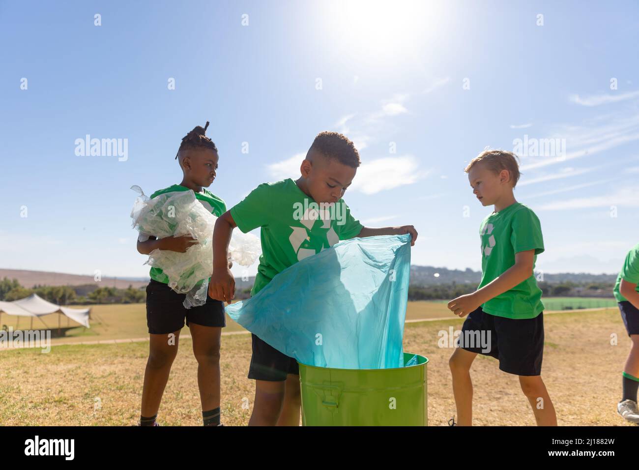 Multirassische Grundschüler, die an sonnigen Tagen Plastik auf dem Schulgelände putzen Stockfoto