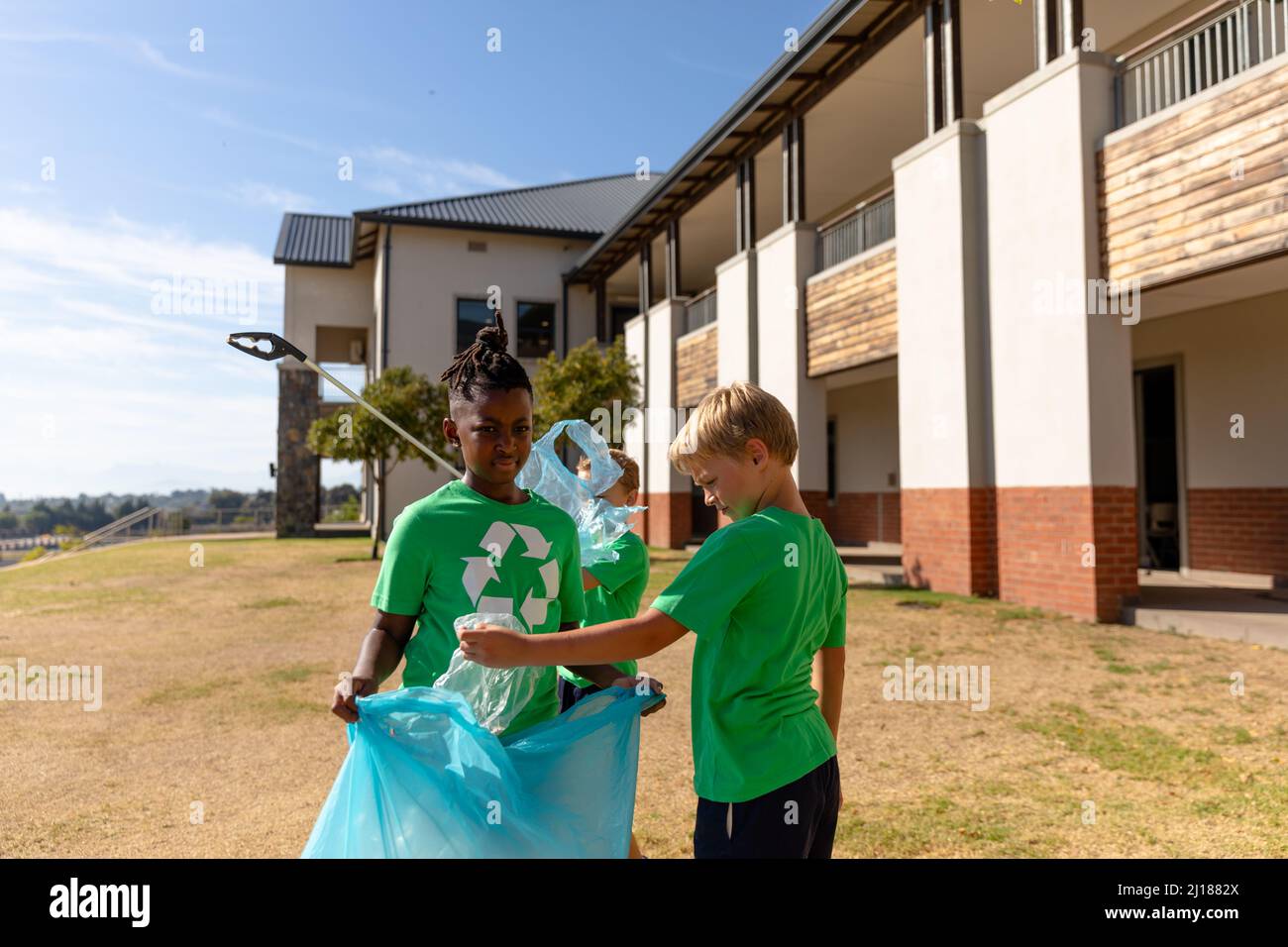 Multirassische Grundschüler sammeln an sonnigen Tagen Plastik in Mülltüten Stockfoto