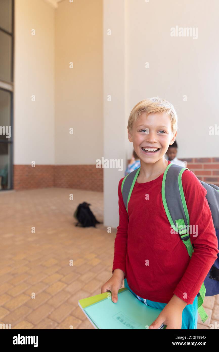 Fröhlicher kaukasischer Grundschüler mit Büchern, die auf dem Schulcampus wegschauen Stockfoto