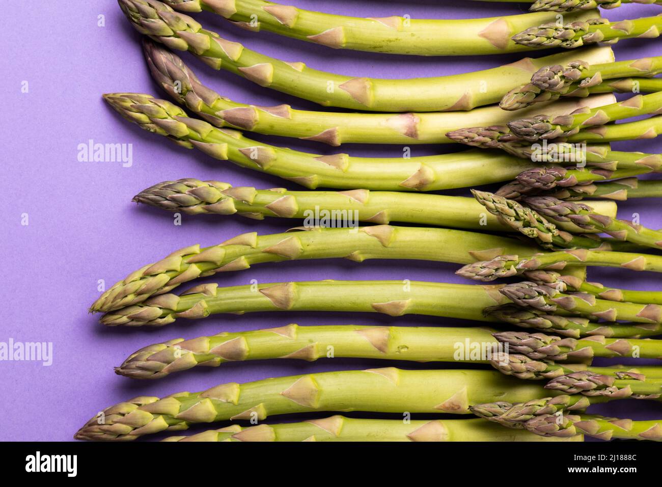 Oben Nahaufnahme von rohem Gemüse mit grünem Spargel vor violettem Hintergrund Stockfoto