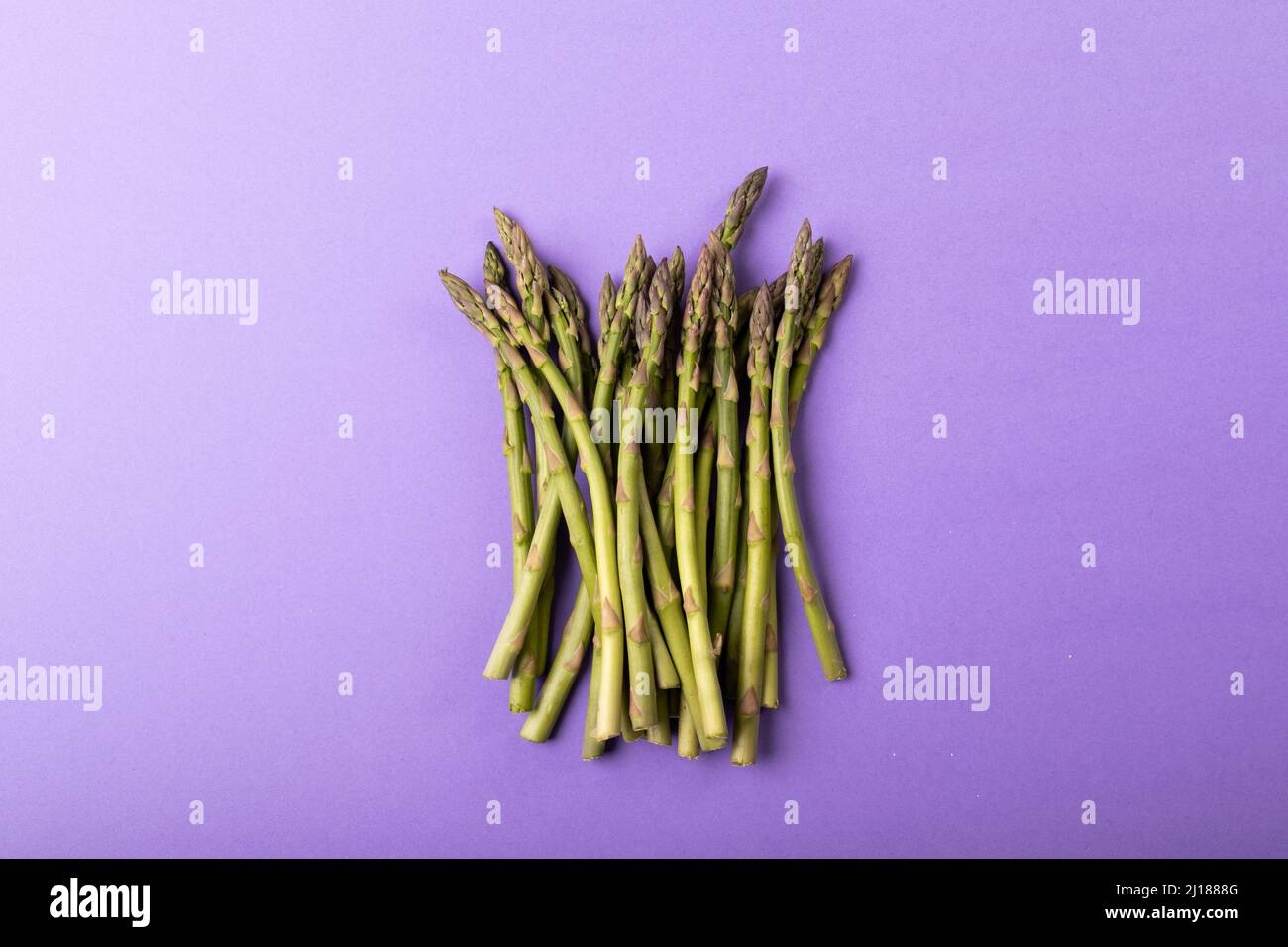 Overhead-Ansicht von rohem Gemüse mit grünem Spargel durch Kopierraum vor violettem Hintergrund Stockfoto