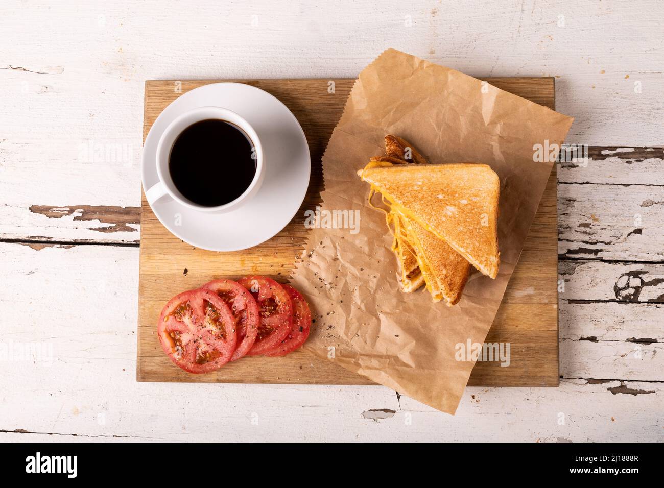 Blick von oben auf das Frischkäse-Sandwich mit Tomatenscheiben und schwarzem Kaffee auf dem Servierbrett Stockfoto
