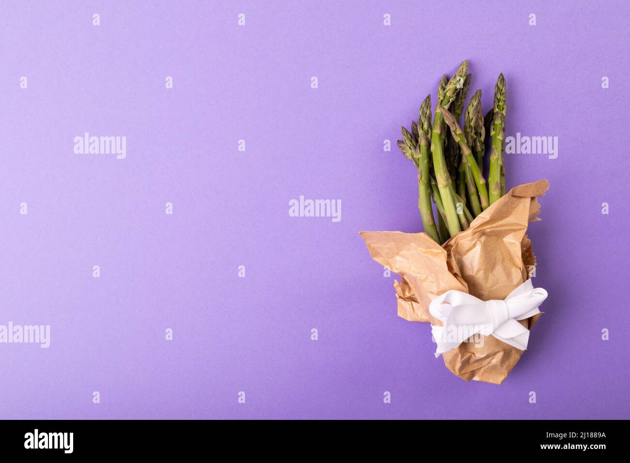 Overhead-Ansicht des Kopierraums durch Spargelbündel in Papier mit Band auf lila Hintergrund gebunden Stockfoto