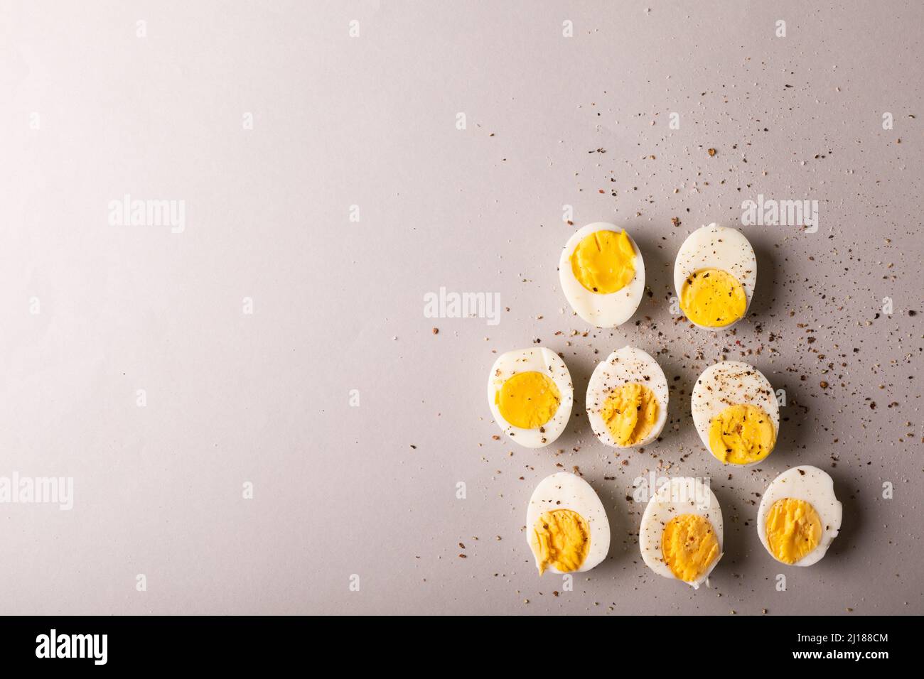 Overhead-Ansicht der Pfefferkornwürze auf gekochten weißen Eiern durch Copy Space auf grauem Hintergrund Stockfoto
