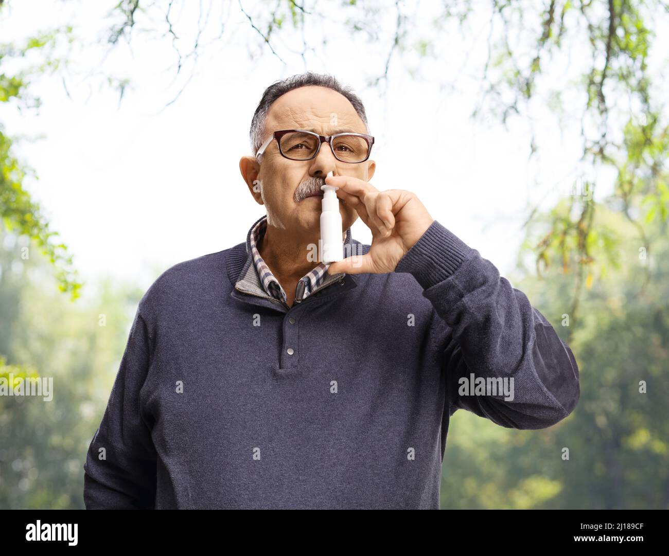 Reifer Mann mit Nasenspray in einem Park mit Bäumen hinter sich Stockfoto