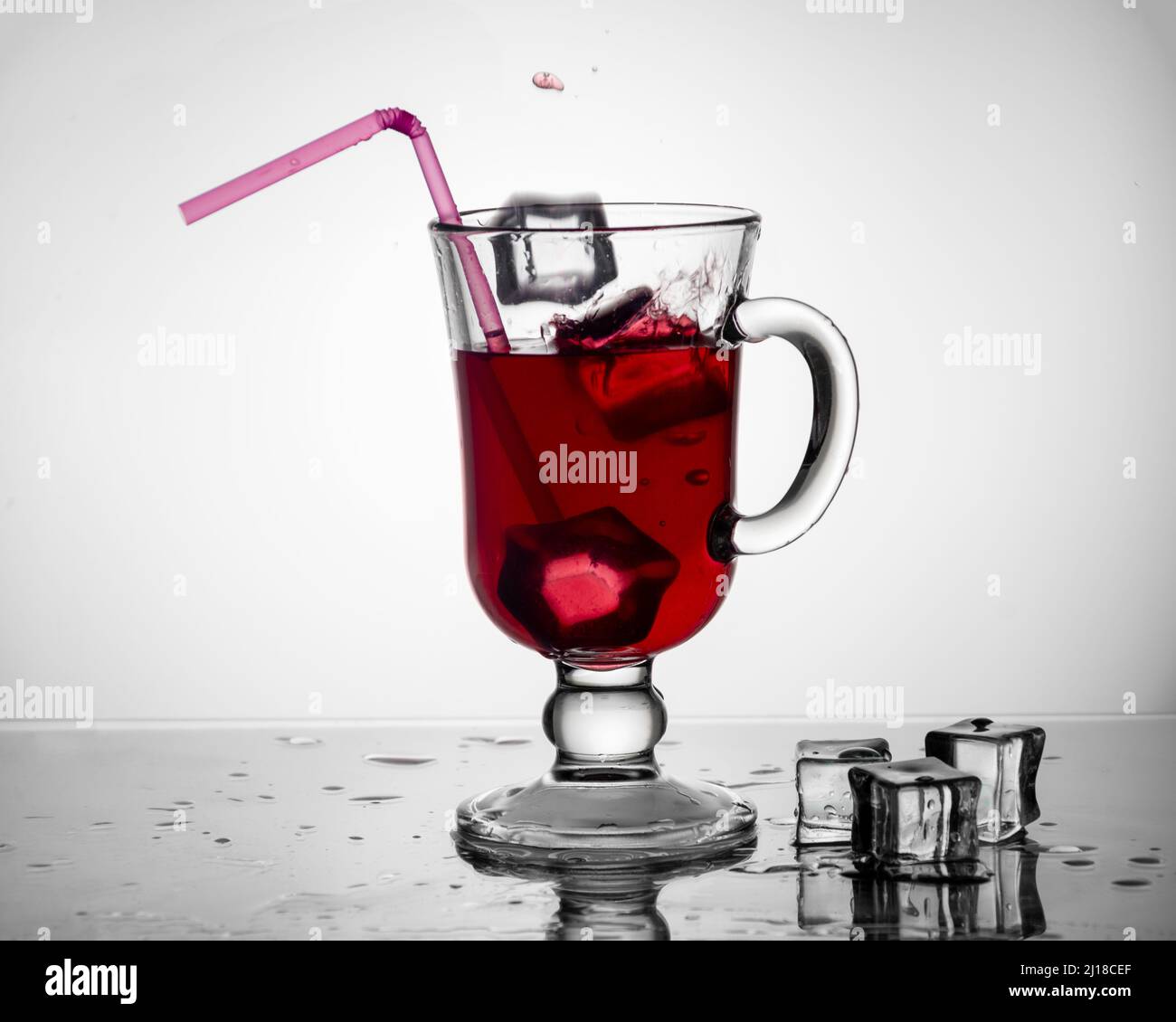 Kalter Tee, Cocktail, Fruchtgetränk in einer hohen Glasschale mit Trinkhalm auf einem Tisch mit Eisstücken auf einem weißen Hintergrund. Sommergetränke Stockfoto