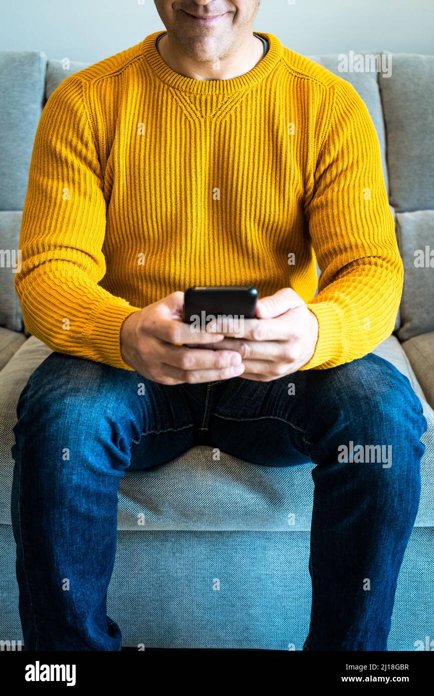 Nahaufnahme eines lächelnden Mannes mit Smartphone auf dem Sofa. Von zu Hause aus verbunden Stockfoto