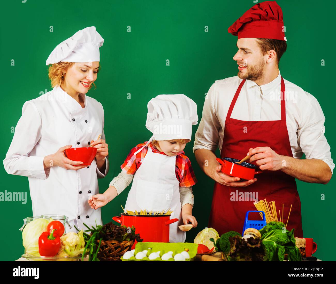 Familie kocht zusammen zu Hause. Niedliches Kind und Eltern im Küchenhut. Gesunder Lebensstil Stockfoto