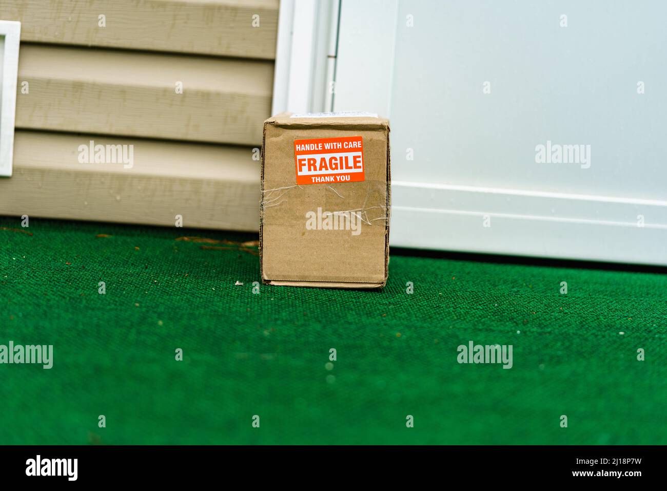 Ein Paket außerhalb einer Wohntür mit einem zerbrechlichen, mit Vorsicht gehandhabten Aufkleber auf dem Karton. Stockfoto
