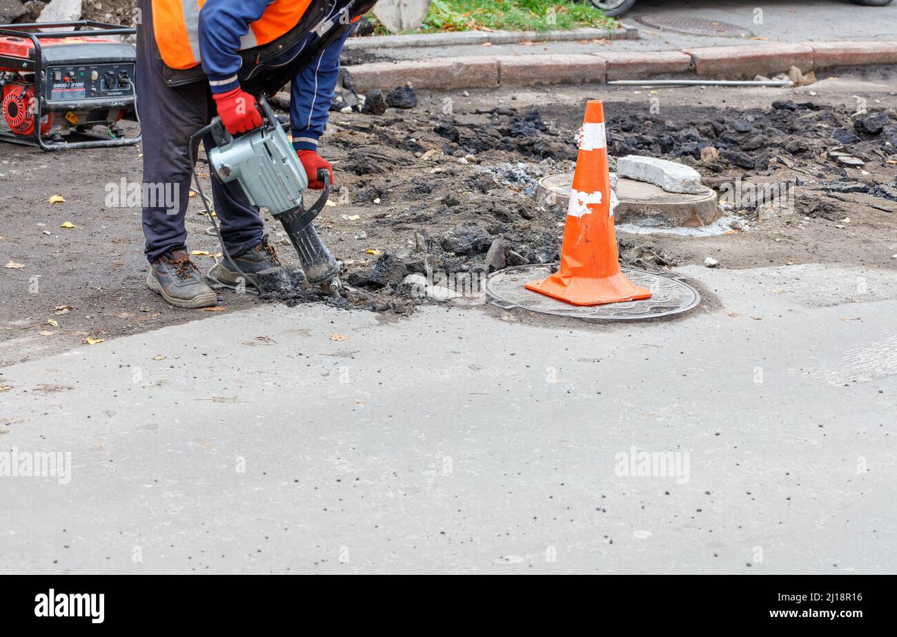 Ein Arbeiter mit einem elektrischen Presshammer bricht den alten Asphalt von der Straße um den Kanalschachtel. Stockfoto