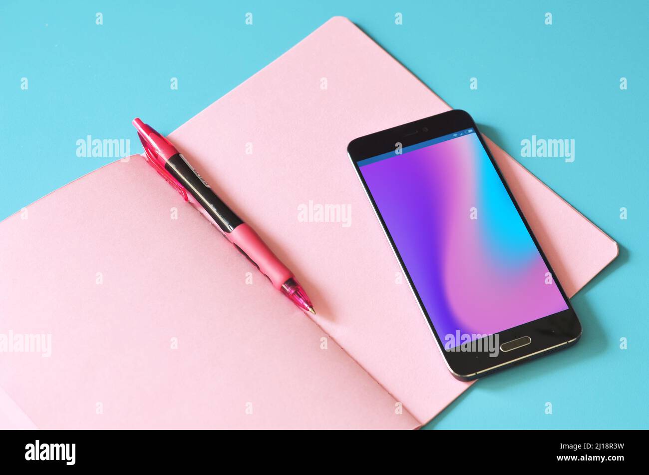 Smartphone und pinkes Notebook auf blauem Tisch. Stockfoto