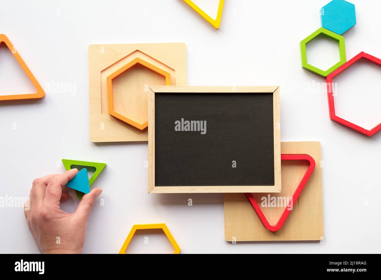 Geometrische Holzfiguren und Tafel. Genestete Holz-Dreiecke und Sechsecke in Regenbogenfarben. Türkisfarbenes Dreieck in menschlicher Hand. Stockfoto