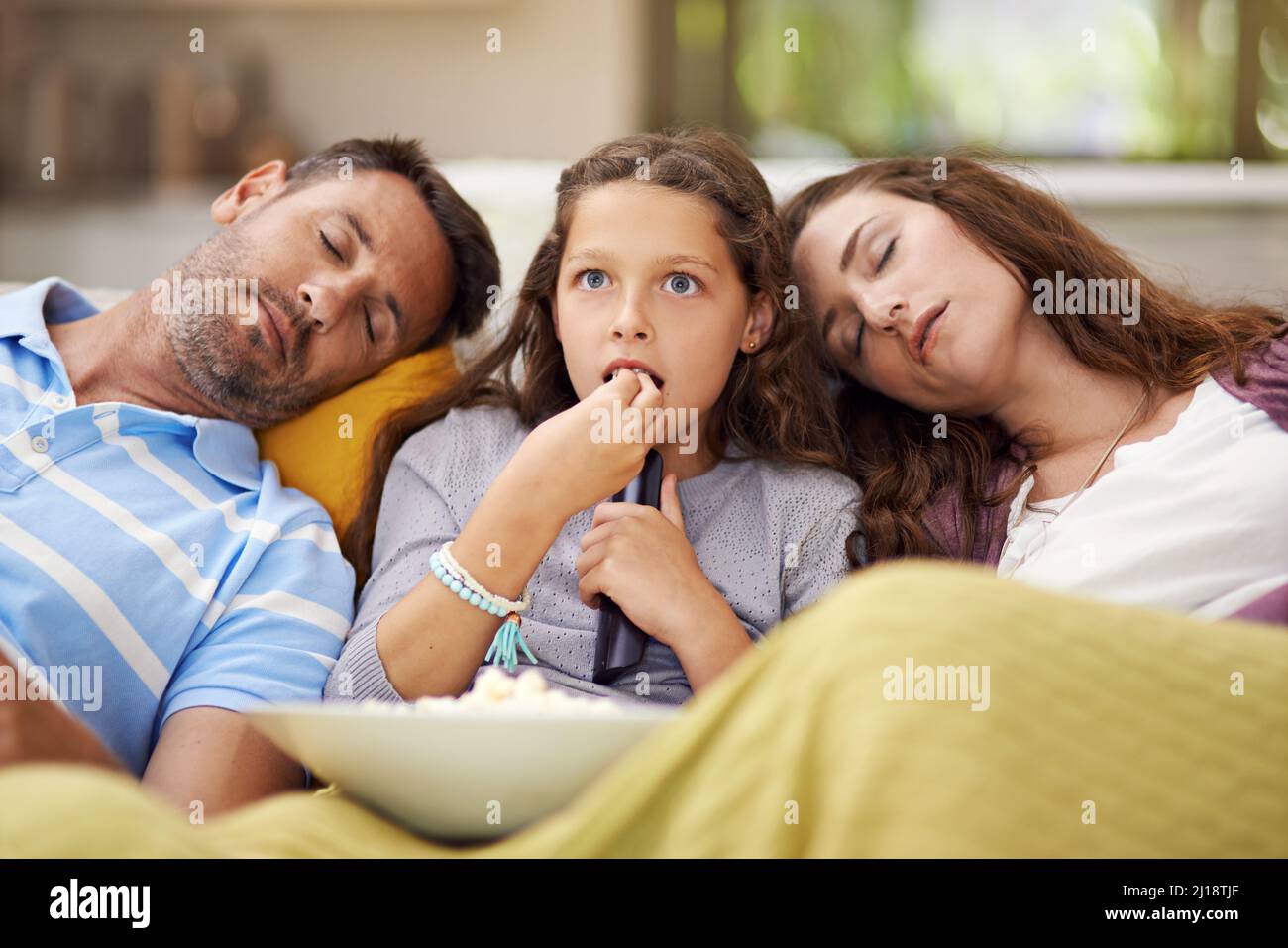 Familienfilmabend. Aufnahme eines Mädchens, das im Wohnzimmer sitzt und einen Film mit ihren Eltern schaut, die neben ihr schlafen. Stockfoto