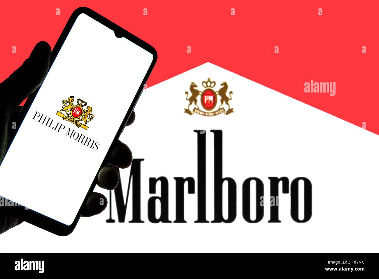 Auf dieser Fotolabbildung ist ein Logo von Philip Morris International zu sehen, das auf einem Smartphone mit einem Marlboro-Logo im Hintergrund angezeigt wird. Stockfoto