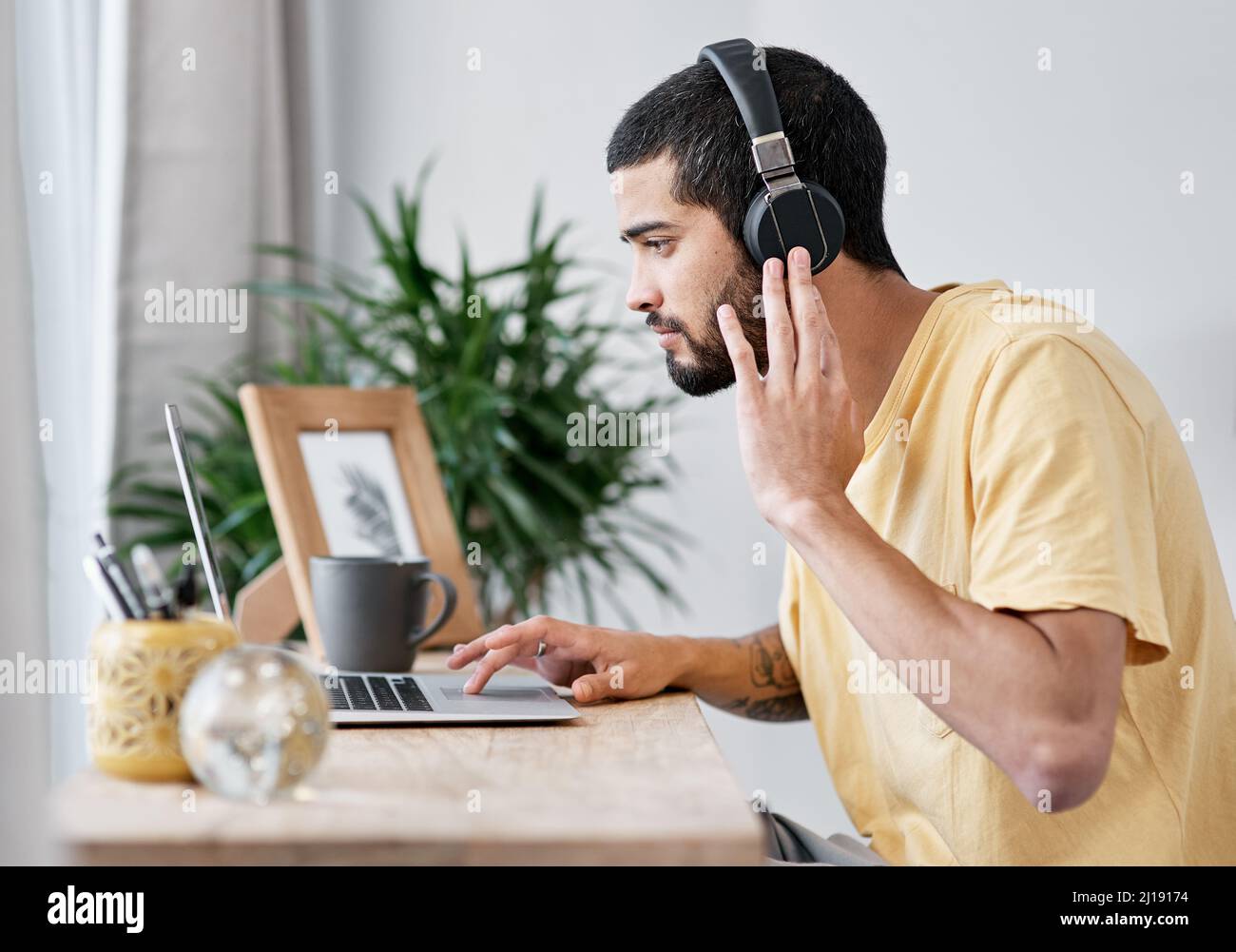 Die besten Kopfhörer mit Geräuschminimierung in der Branche. Aufnahme eines jungen Mannes, der einen Laptop und Kopfhörer benutzt, während er von zu Hause aus arbeitet. Stockfoto