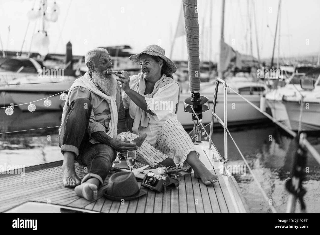 Ältere Paare haben Spaß beim Essen Früchte auf dem Segelboot - Fokus auf Frau Gesicht - Schwarz-Weiß-Ausgabe Stockfoto