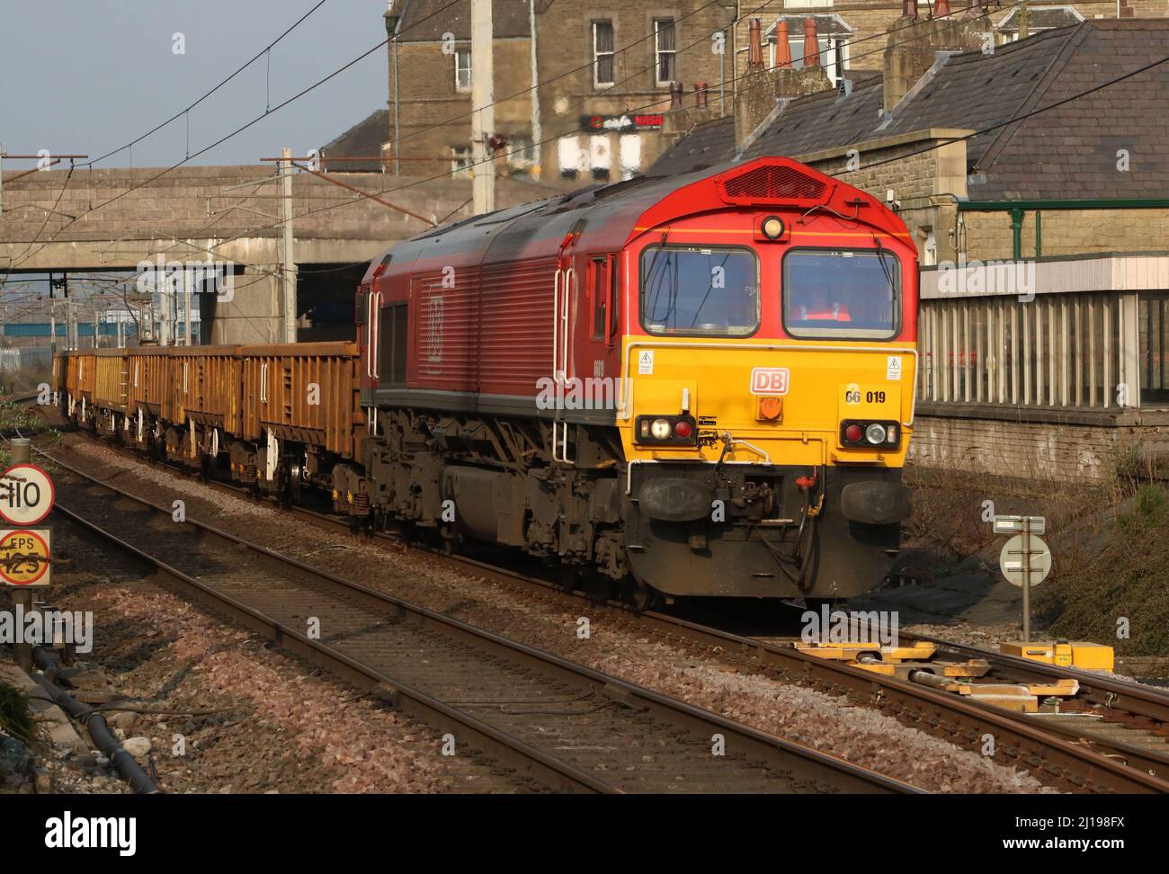 Diesel-elektrische Lokomotive der Baureihe 66, Nummer 66019, in roter DB-Laderaumgebung, die am Mittwoch, 23.. März 2022, Carnforth auf der WCML durchquert. Stockfoto