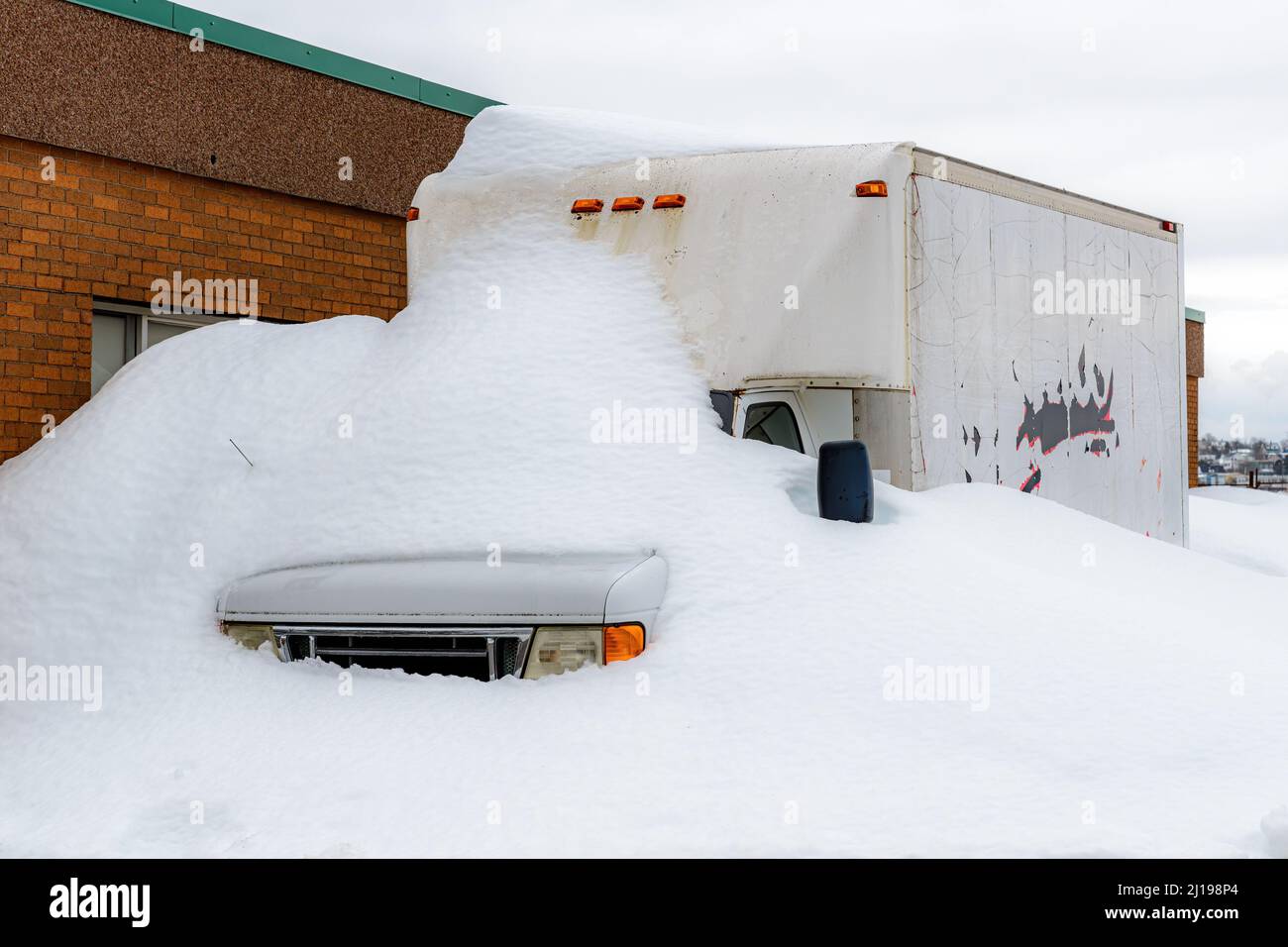 Ein generischer Lieferwagen, der teilweise von Schnee vergraben ist, neben einem Ziegelgebäude. Bewölktes Himmel. Fahrzeug ist nicht identifizierbar. Stockfoto