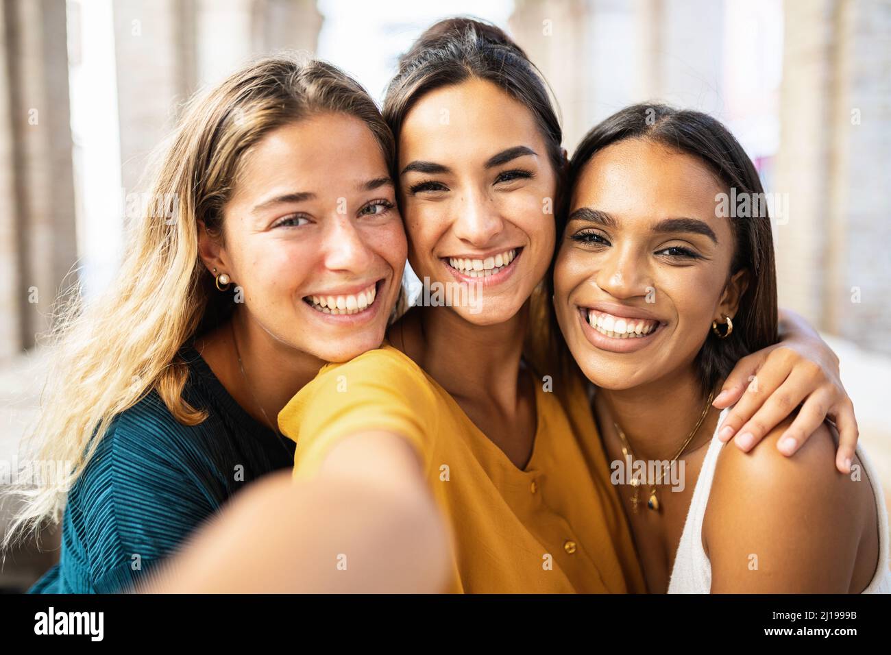 Drei multiethnische junge Freundinnen, die gemeinsam lachen und Selfie im Freien machen Stockfoto
