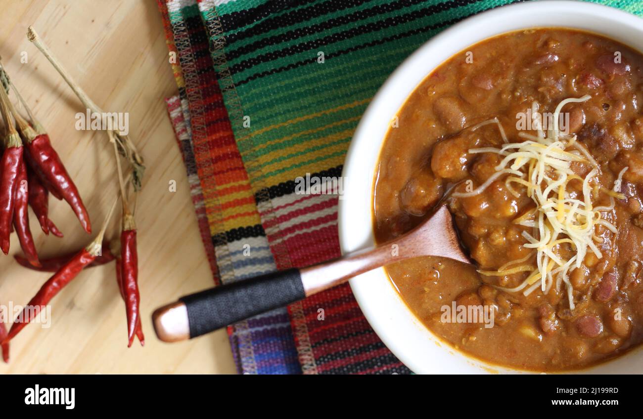 Schüssel Chili mit Pinto-Bohnen auf dem Tisch mit Paprika, Gewürzen und trockenen Bohnen im Hintergrund Stockfoto