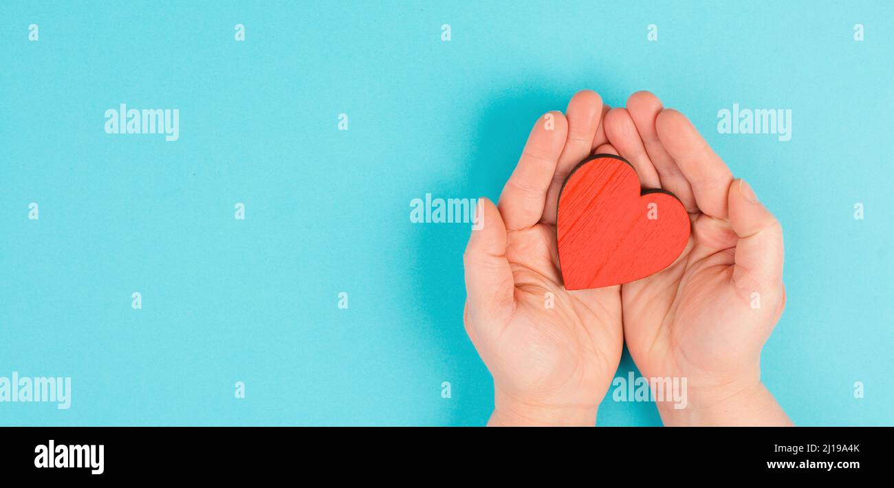 Frau hält ein rotes Herz in der Hand, blauer Hintergrund, Kopierraum, Liebe und Nächstenliebe Symbol, Hoffnung Konzept Stockfoto